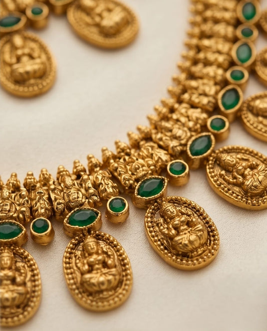 Gold necklace with green gemstones on a light background