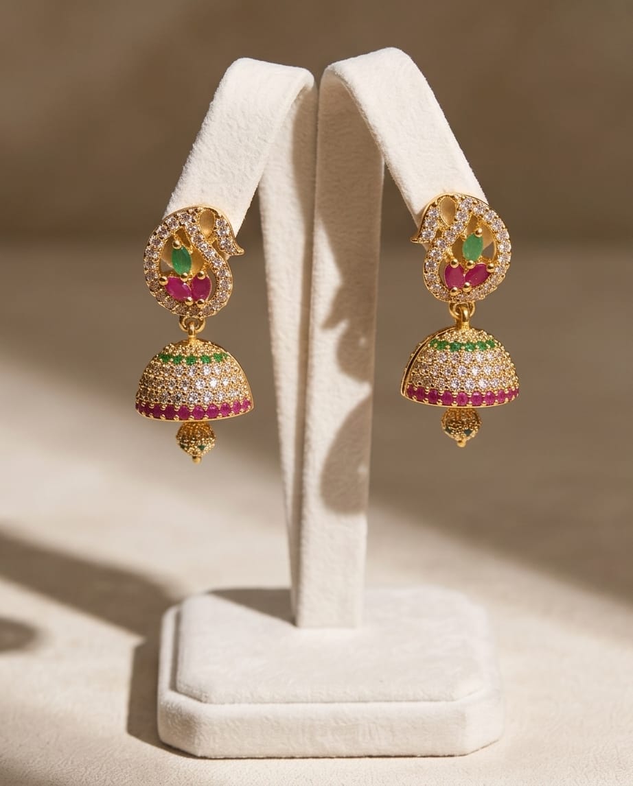 Gold earrings with colorful stones on a white stand against a beige background