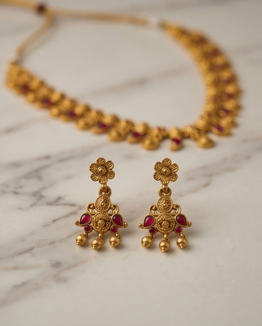 Gold earrings with red stones on a marble surface