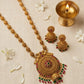 Gold necklace with intricate design and gemstones on a beige background with flowers and a small lamp.