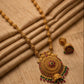 Gold necklace with intricate design and red and green gemstones on a beige fabric background