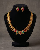 Gold necklace with red and green gemstones and matching earrings on a black stand against a gray background