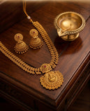 Gold necklace and earrings set on a wooden surface with a small brass lamp.