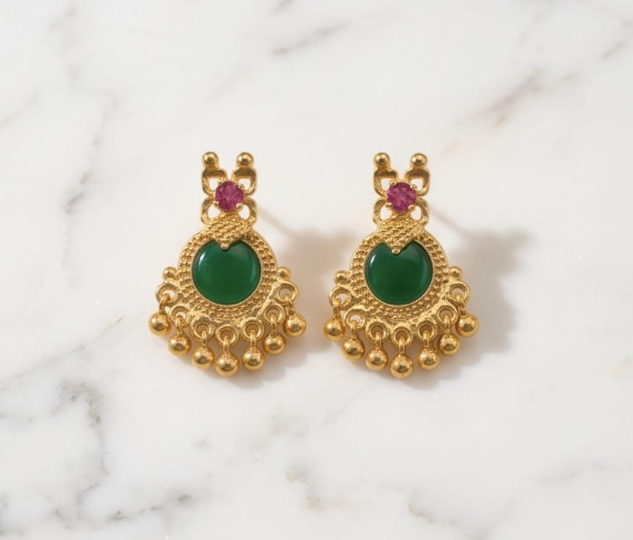 Gold earrings with green gemstones on a marble background