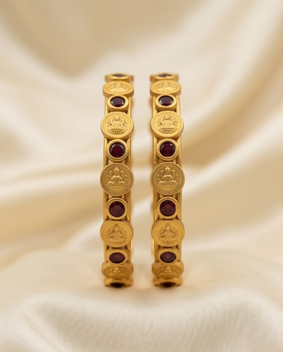 Pair of gold bangles with red stones on a beige fabric background