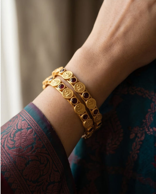 Gold bracelet with embedded stones on a wrist, wearing a patterned garment.