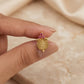 Gold pendant with pink gemstones held between fingers against a beige fabric background