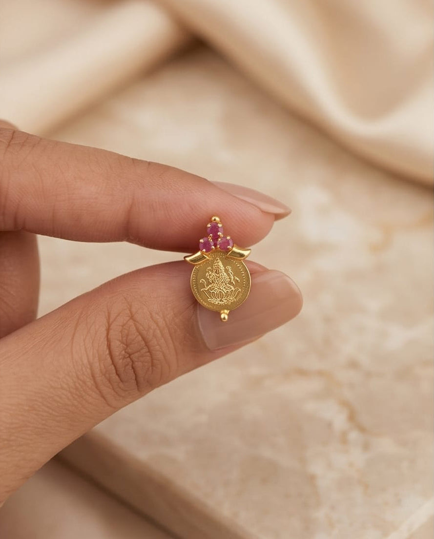 Gold pendant with pink gemstones held between fingers against a beige fabric background