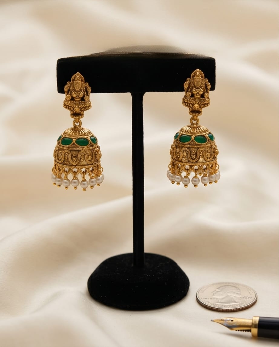 Gold earrings with green stones on a black stand against a beige background