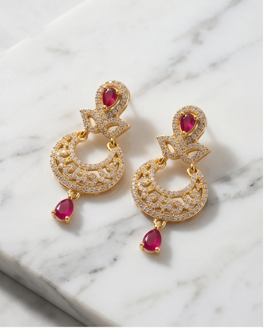 Gold earrings with red gemstones on a marble surface