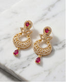 Gold earrings with red gemstones on a marble surface
