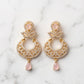 Gold earrings with pink teardrop stones on a marble background