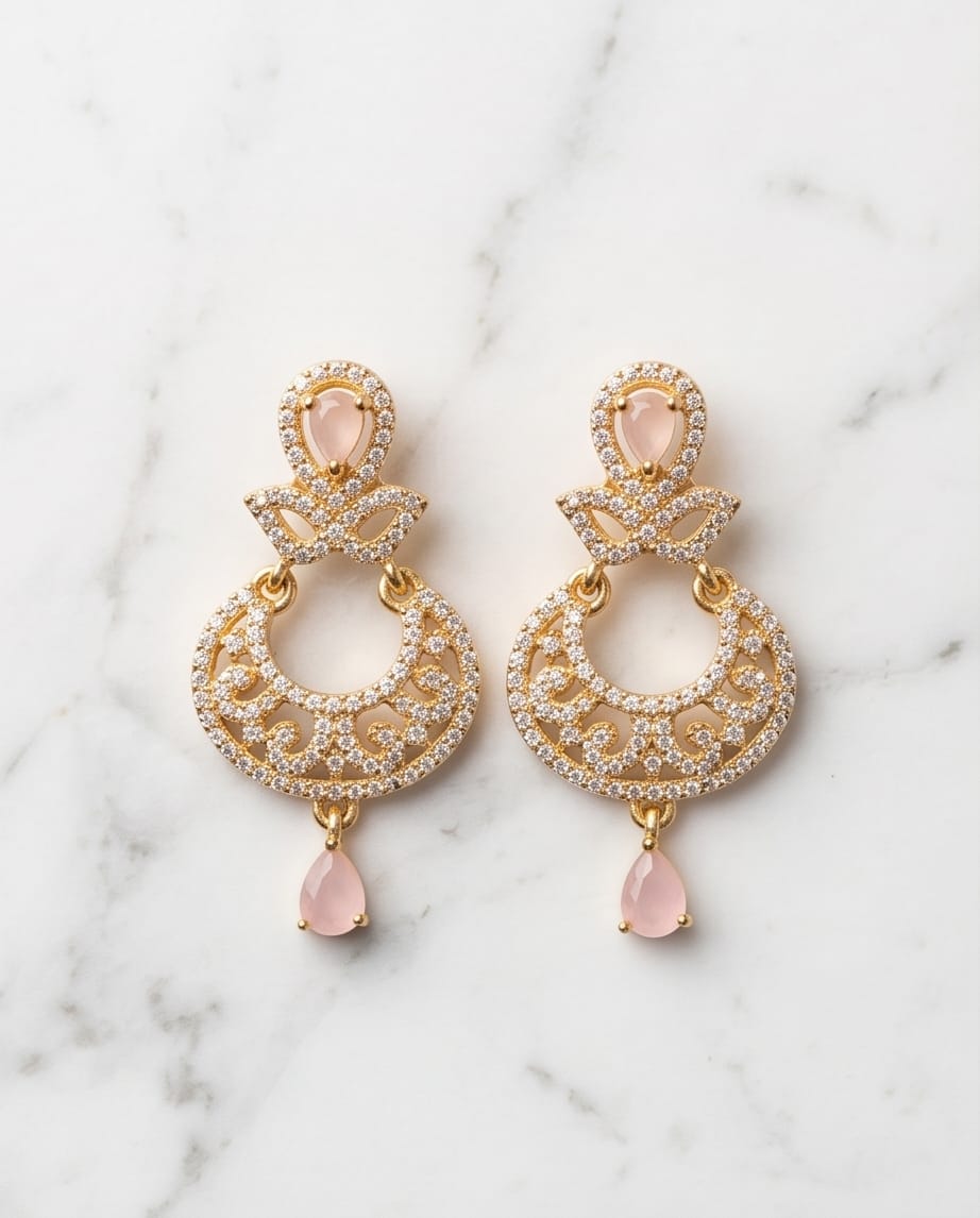 Gold earrings with pink teardrop stones on a marble background