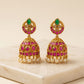 Pair of gold earrings with pink and green gemstones on a beige surface