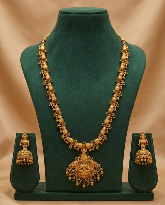Gold necklace and earrings set on a green mannequin against a beige background