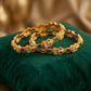 Gold bracelets with gemstones on a green cushion