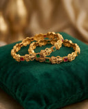 Gold bracelets with gemstones on a green cushion