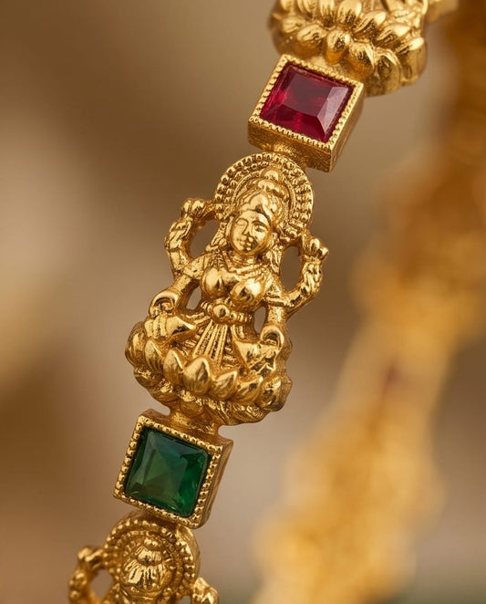 Gold necklace with a figure and embedded red and green gemstones on a blurred gold background
