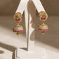 Gold earrings with colorful stones on a white stand against a beige background