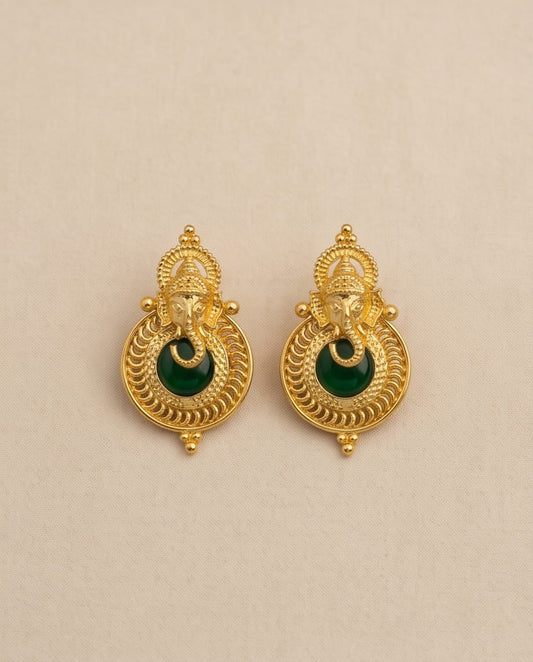 Gold earrings with green gemstones on a beige background