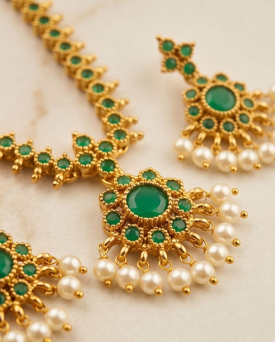 Gold jewelry with green stones and pearls on a light background