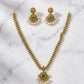 Gold necklace with green stones and pearl earrings on a marble background