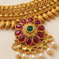 Gold necklace with red gemstones and pearl drops on a beige background