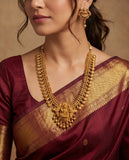 Woman wearing a maroon saree with gold jewelry including a necklace and earrings.