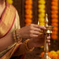 Person in traditional attire holding a brass lamp with a blurred decorative background