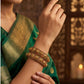 Woman wearing gold bangles on a green saree with a warm background