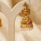 Gold jhumka earrings with pearls and a red gemstone on a beige stand.