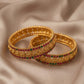 Pair of gold bangles with gemstones on a beige fabric background