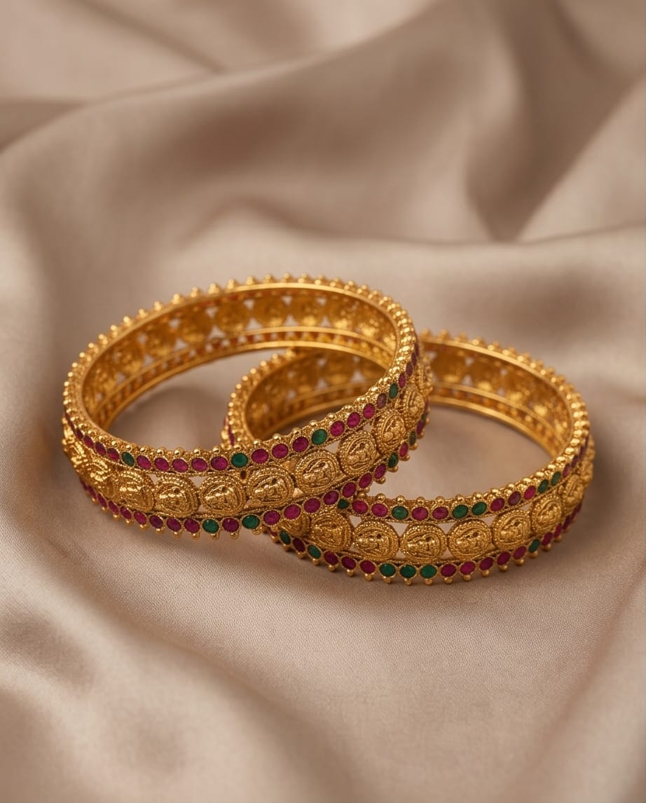 Pair of gold bangles with gemstones on a beige fabric background