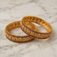 Two gold bangles with gemstones on a marble surface