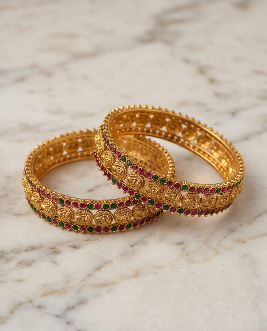 Two gold bangles with gemstones on a marble surface