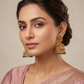 Woman wearing gold and green earrings with a neutral background