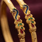 Gold bangles with intricate designs and colored stones on a dark background