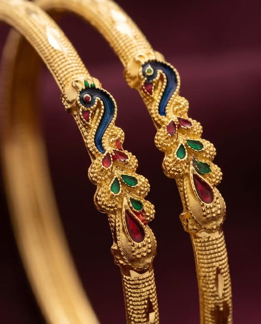 Gold bangles with intricate designs and colored stones on a dark background