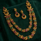 Gold necklace with red and green gemstones on a dark green fabric background