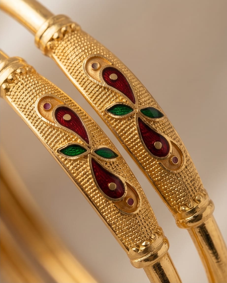 Gold bangles with red and green gemstones on a beige background