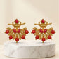 Pair of gold earrings with red beads on a marble stand against a beige background