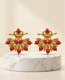 Pair of gold earrings with red beads on a marble stand against a beige background