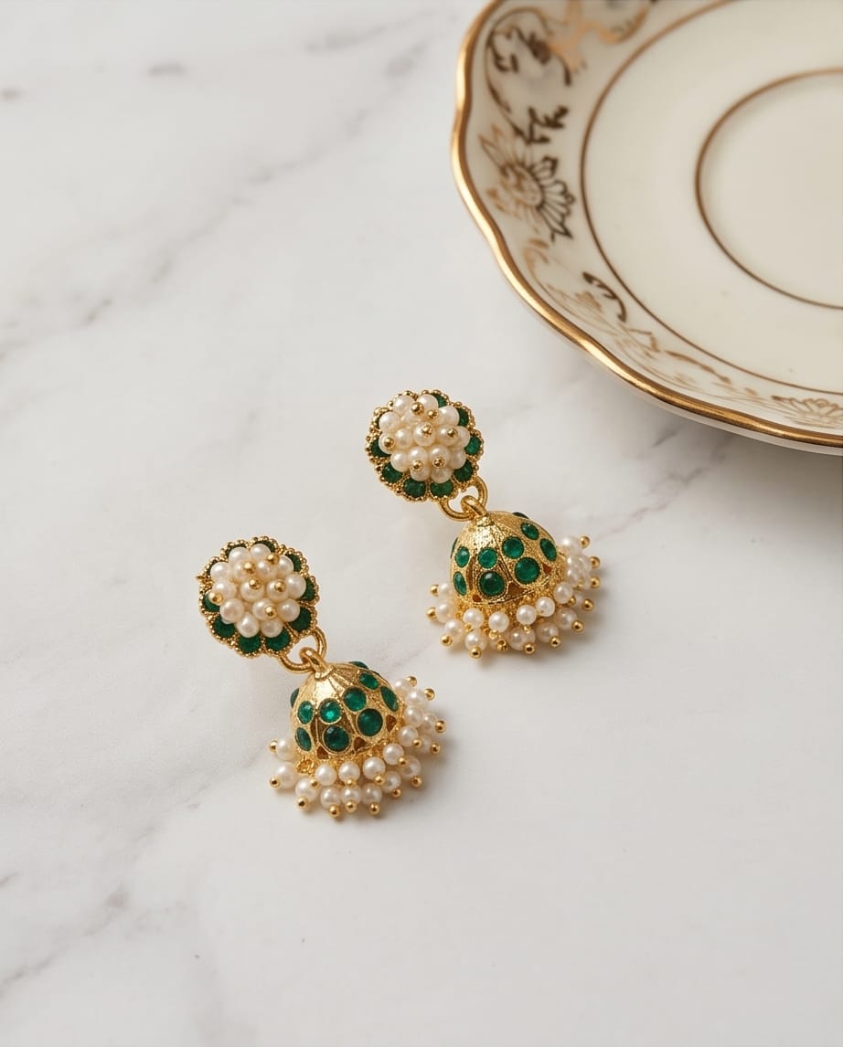 Pair of gold earrings with green and pearl details on a marble surface.