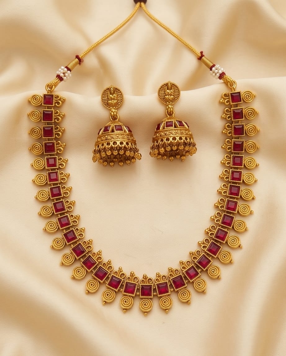 Gold necklace with red stones and matching earrings on a beige fabric background