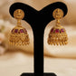 Gold earrings with red stones on a black stand against a beige background