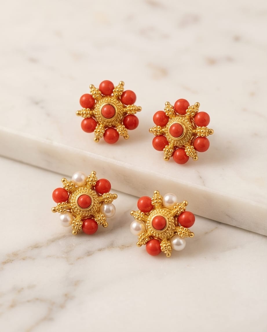 Gold earrings with red and pearl stones on a marble surface