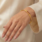 Gold bracelet with red stones on a hand against a beige background