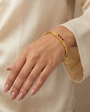 Gold bracelet with red stones on a hand against a beige background