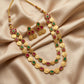 Gold necklace and earrings with red and green stones on a beige fabric background