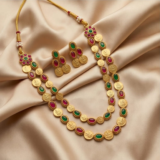 Gold necklace and earrings with red and green stones on a beige fabric background